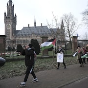 Une dizaine de jeunes manifestants brandissent pancartes et drapeaux palestiniens devant un édifice.