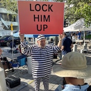 Un homme habillé en prisonnier brandit une pancarte réclamant l'emprisonnement de Donald Trump.