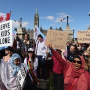 Des manifestants qui dressent des pancartes disant «Laissez nos enfants tranquilles» côtoient devant le parlement d'Ottawa des gens tenant des pancartes qui disent «Les droits trans sont des droits de la personne».