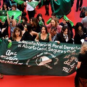 Des militantes tiennent une banderole et brandissent des foulards sur le tapis rouge à Cannes.