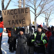 Une femme tient un pancarte sur laquelle on peut lire «Vacciné et tanné».