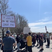 Des dizaines de personnes, dont certaines brandissent des pancartes, sont rassemblées devant la caisse Desjardins à Saint-Gabriel-de-Rimouski.