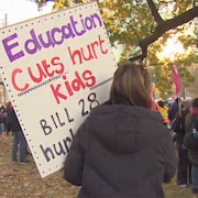 Une manifestante tient une pancarte qui accuse le gouvernement de faire des coupes en éducation.