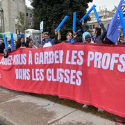 Des personnes qui tiennent une banderoles où il est écrit : aidez-nous à garder les profs dans les classes. 