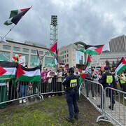 Des manifestants brandissant des drapeaux palestiniens devant un policier derrière une clôture. 