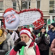 Une manifestante tient une pancarte avec un père Noël qui dit : « La tâche des profs n'est pas un cadeau, monsieur Legault! Ne les prenez plus pour des lutins! »