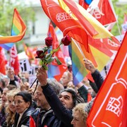 Dans une foule de manifestants qui tiennent des drapeaux du Parti socialiste espagnol et des drapeaux L G B T Q +, un homme tient des roses à bout de bras.