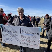 Une femme avec une pancarte avec des inscriptions en anglais, et derrière, se trouvent plusieurs personnes.