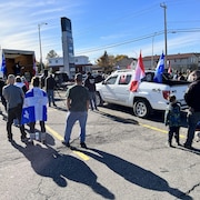 Des manifestants écoutent un discours en brandissant des drapeaux du Québec et du Canada.