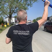 Un homme que l'on voit de dos brandit un bras et porte un chandail avec l'inscription «couper en éducation, c'est irresponsable». 