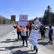Un groupe d'une dizaine de personnes au bord d'une route tient des pancartes disant non au dépotoir. 