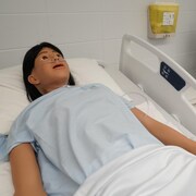 Un mannequin intelligent couché sur un lit d'hôpital avec à sa gauche un moniteur.