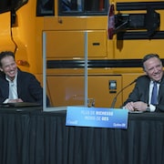 Marc Bédard et François Legault, souriants et assis durant une conférence de presse.