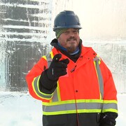Marc Lepire, l'artisan derrière le palais de glace de Bonhomme Carnaval en tenu de construction, devant un mur de glace. 