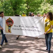 Deux personnes tiennent une bannière avec les mots «Foyer pour femmes autochtones de Montréal» dessus. D'autres personnes les suivent à la marche derrière. 
