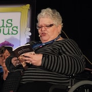 Margot Lemire sur scène, dans un fauteuil roulant, lisant un livre au public.