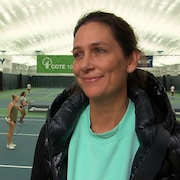 Marie-Ève Pelletier sourit devant la caméra avec des terrains de tennis et des joueurs en arrière-plan.