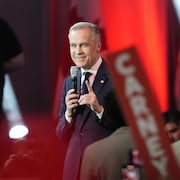 Mark Carney sourit avec le doigt levé.