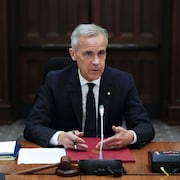 Mark Carney signe un document devant la presse.
