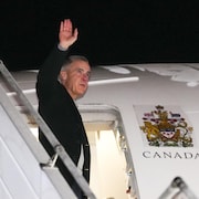 Le premier ministre Mark Carney salue les gens en entrant dans un avion.