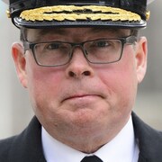 Gros plan sur le visage du vice-amiral des Forces armées canadiennes Mark Norman qui porte un képi militaire et des lunettes.