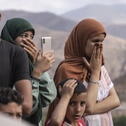 Deux femmes et un homme, la main sur le nez et la bouche, observent le travail des secouristes dans une région montagneuse.