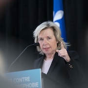 Martine Biron en conférence de presse lève l'index en regardant l'auditoire.