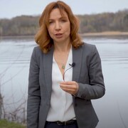 Une femme en veston se tient devant un lac.