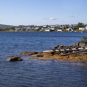 Un petit village côtier avec des habitations tout près de l'eau, photographié d'une autre rive, en été, par temps clair.