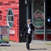 Un homme portant un masque marche sur le trottoir et passe devant un pizzeria.           