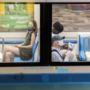 Dans un wagon de métro, quatre personnes portent un masque; un homme n'en porte pas.