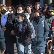 Un groupe de gens marchent sur un trottoir. Une personne est à vélo.