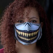 Une femme porte un masque sur lequel est imprimé une bouche ouverte et de grandes dents. 