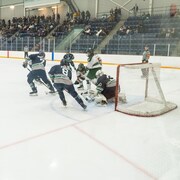 Deux équipes de hockey se disputent la rondelle sur une patinoire près d’un filet de gardien de but.