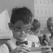 Un garçon, masque de papier sur les yeux, s'amuse avec des blocs dans une classe de maternelle.