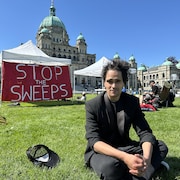 Mathieu Pacheco Ramirez, assis sur la pelouse devant l'Assemblée législative, à Victoria, le 8 mai 2024.
