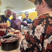 Homme qui sert du jambon dans l'assiette d'une femme, le 3 décembre 2023 à Saint-Denis en Saskatchewan.