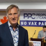 Maxime Bernier pose devant le drapeau du Canada à côté d’une affiche du Parti populaire du Canada.  
