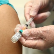 Un infirmier tient une seringue et s'apprête à vacciner quelqu'un dans le bras gauche.