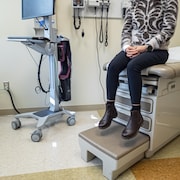 Les deux pieds d'une femme portant des bottes ne touchent pas le sol, alors qu'elle est assise sur la table d'examen chez un médecin.