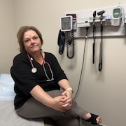 Stéthoscope au cou et mains croisées, la Dre Shannon Dowler est assise sur une table de consultation dans une clinique médicale.
