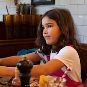 Une enfant assise à une table de restaurant.