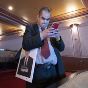 Un partisan caquiste regarde son téléphone cellulaire, une pancarte de François Legault sous le bras.
