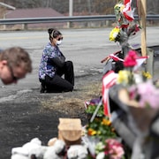 Une femme agenouillée devant un mémorial composé de fleurs autour d'un garde-fou en bordure de l'autoroute.