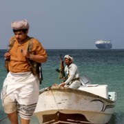 Quatre hommes armés se tiennent près d'une barque.