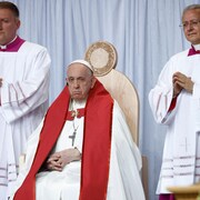 Le pape François, assis, entouré de deux concélébrants 