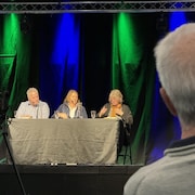 Trois personnes assises à une table donnent une conférence. 