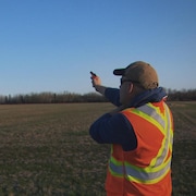 Un homme portant un dossard debout dans un champ avec un fusil dans les mains.