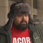 Michael Cuadra en entrevue avec une tuque à la tête et un chandail de l'organisme ACORN devant l'hôtel de ville de Toronto.