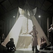 Des acteurs déguisés en Autochtones sont devant un tipi sur une scène.